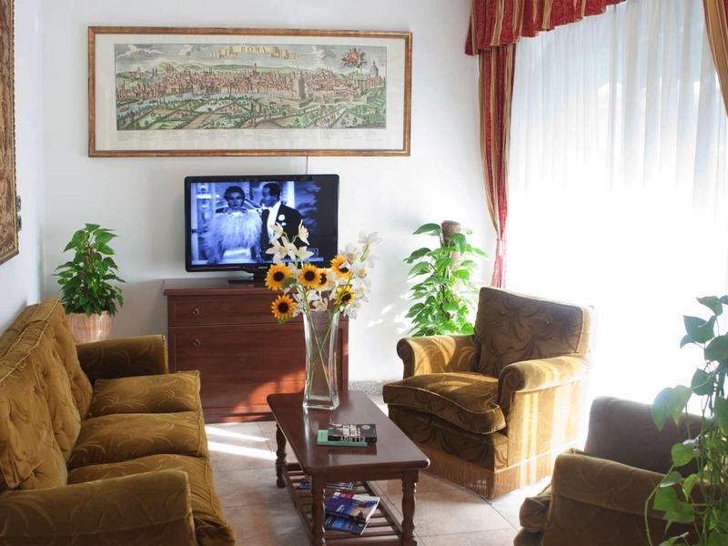 Světý obývací pokoj s hnědými křesly, pohovkou, televizí a rostlinami u velkého okna.