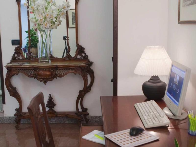 Stůl s počítačem a starožitná zrcadlová konzola s květinami v světlé místnosti.