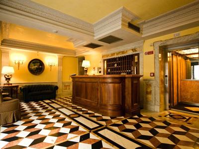 Hell beleuchteter Empfangsbereich mit braunem Holztresen und schwarz-weiß gemustertem Boden.