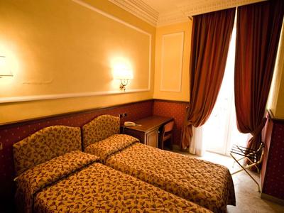 Hotelzimmer mit zwei Einzelbetten, Tisch, Stuhl und großen Vorhängen an einem Balkonfenster.