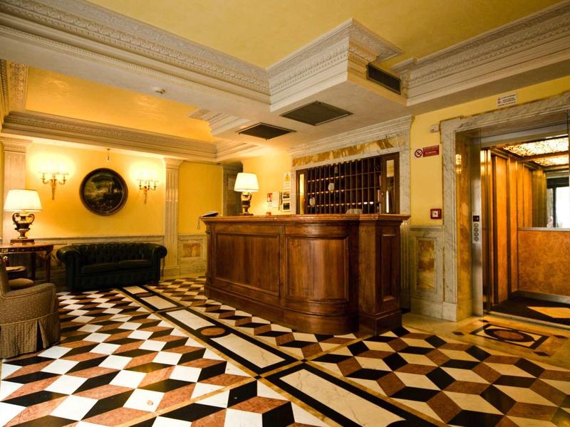 Hell beleuchteter Empfangsbereich mit braunem Holztresen und schwarz-weiß gemustertem Boden.