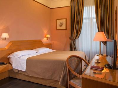 Camera d'hotel accogliente con letto matrimoniale, scrivania, sedia e tende alla finestra.