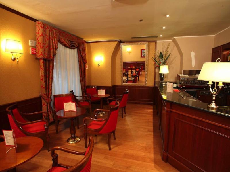 Przytulny bar hotelowy z czerwonymi fotelami, drewnianą podłogą i miękkim oświetleniem.