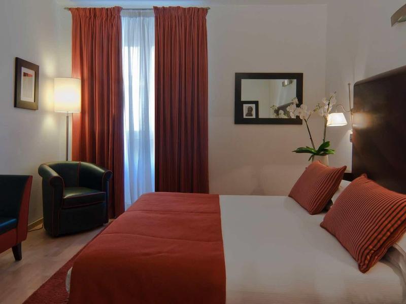 Gezellige hotelkamer met tweepersoonsbed, warme rode tinten en zithoek.