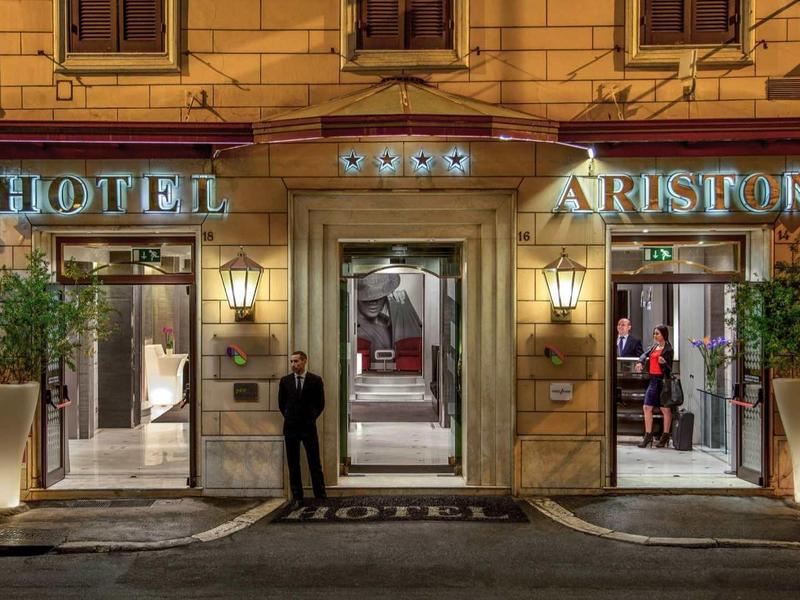 Elegante hotelentree 's nachts met verlichting en twee grote planten in potten.