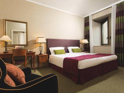 Chambre d'hôtel élégante avec lit double, bureau, chaise et éclairage chaleureux.