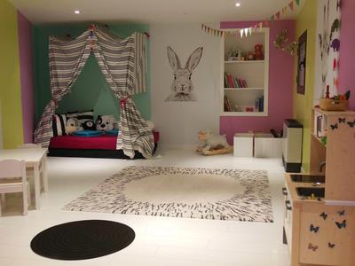 Salle de jeux pour enfants avec murs colorés, tapis, maison de poupée et décoration murale lapin.