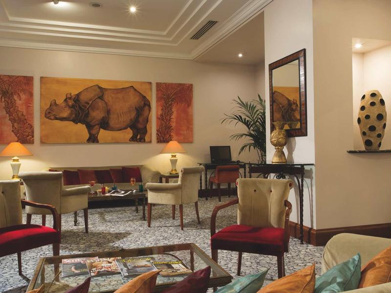 Hall d'hôtel élégant avec des fauteuils confortables, tapis coloré et œuvre décorative de rhinocéros au mur.