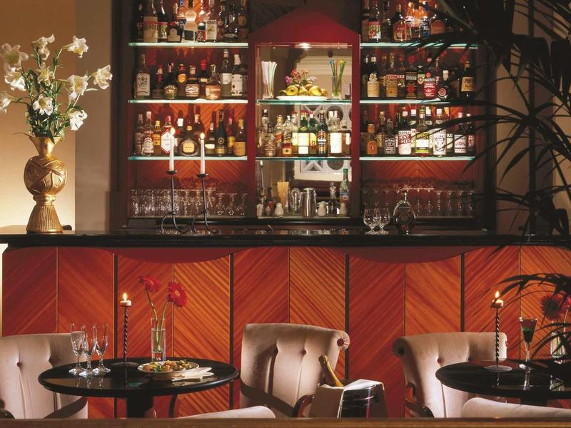 Bar d'hôtel élégante avec bois foncé, étagères pleines de bouteilles et fauteuils confortables.