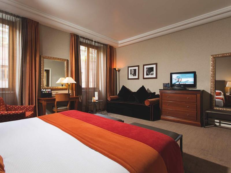 Chambre d'hôtel confortable avec lit double, coin salon et télévision aux tons chauds.