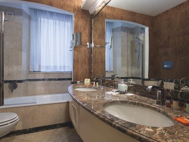 Salle de bains moderne avec plan de travail en marbre, grands miroirs et baignoire avec paroi en verre.