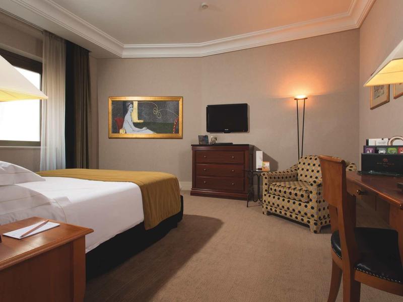 Chambre d'hôtel confortable avec lit, bureau, fauteuil et télévision.