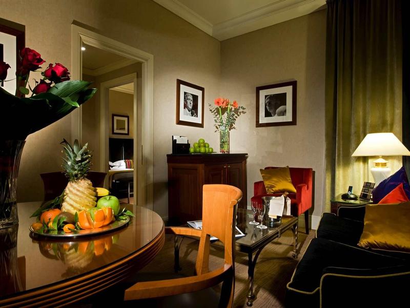 Salon élégant avec rideaux foncés, fleurs fraîches et fruits sur une table en bois.