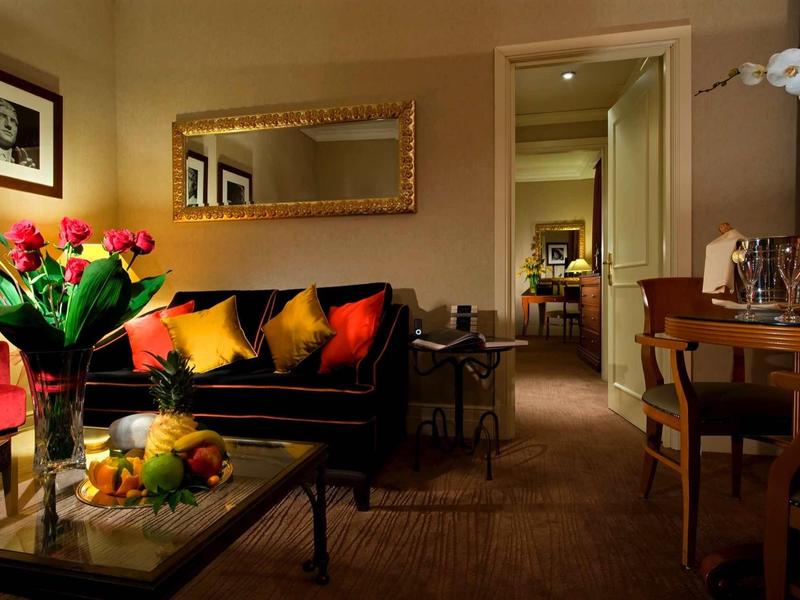 Salon chaleureux avec canapé noir, coussins colorés et table avec fruits et fleurs.