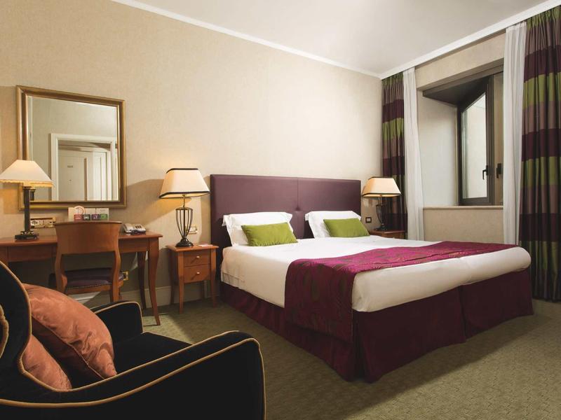 Chambre d'hôtel élégante avec lit double, bureau, chaise et éclairage chaleureux.