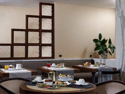 Prosta hotelowa sala z stołami, śniadaniem i dekoracyjnymi ścianami.