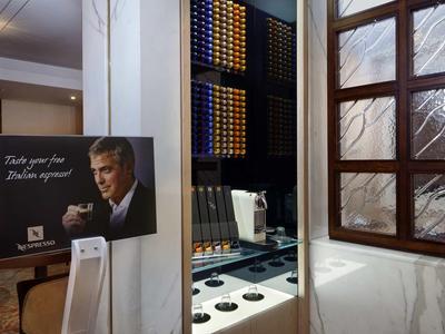 Nowoczesna stacja kawowa z ekspresem kapsułkowym i ścianą ekspozycyjną w jasnym pokoju z drewnianym oknem.