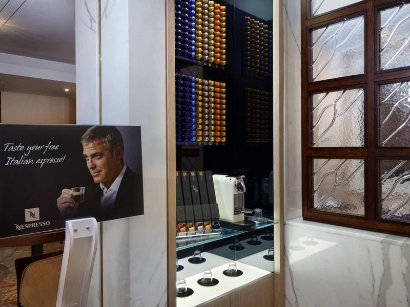 Nowoczesna stacja kawowa z ekspresem kapsułkowym i ścianą ekspozycyjną w jasnym pokoju z drewnianym oknem.