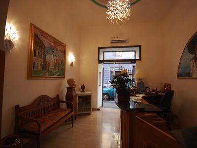 Innenraum mit Sitzbank, Gemälden an den Wänden und Pflanzen, Eingang mit Glas- und Holztür.