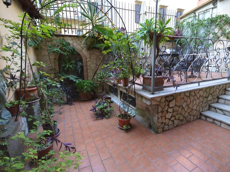 Innenhof mit Terrakottaboden, Pflanzen in Töpfen, Treppe und dekorativem Metallgeländer.