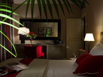 Camera d'hotel accogliente con una sedia rossa, scrivania e luce calda.