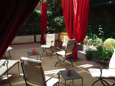 Příjemná venkovní zóna s židlemi, stolem a červenými závěsy v zahradním hotelu.