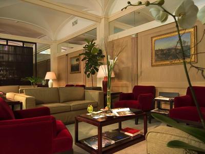 Pohodlný hotelový salonek s červenými křesly, hnědou pohovkou a stylovými dřevěnými stoleky.