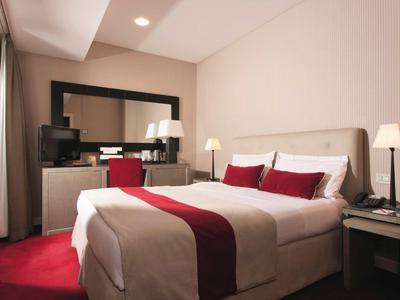 Moderní hotelový pokoj s manželskou postelí, červeným kobercem a velkým zrcadlem.