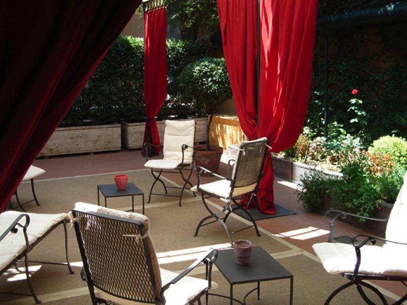 Příjemná venkovní zóna s židlemi, stolem a červenými závěsy v zahradním hotelu.