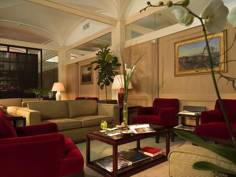 Pohodlný hotelový salonek s červenými křesly, hnědou pohovkou a stylovými dřevěnými stoleky.
