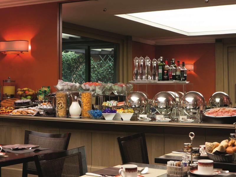 Bufet s různými jídly a nápoji v hotelové restauraci s červenými zdmi.