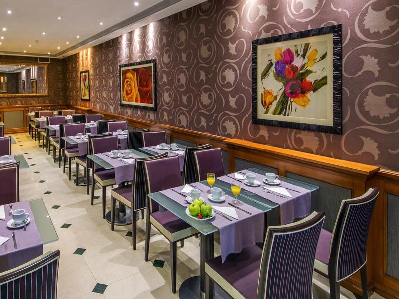 Elegant restaurant with purple chairs, tables with tablecloths, and colorful floral painting on the wall.