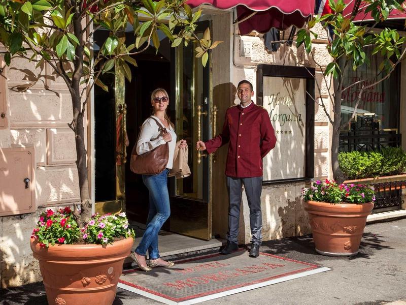 A hotel staff member holds the door open for a woman at the entrance.