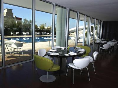 Modernes Café mit weißen und grünen Stühlen, runden Tischen und großen Glasfenstern zum Außenbereich.