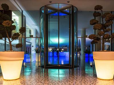 Eingangsbereich eines modernen Hotels mit beleuchteten Pflanzgefäßen und drehbarer Glastür.