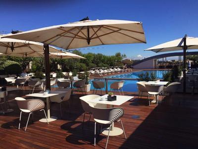 Outdoor-Café mit weißen Tischen und Stühlen, Sonnenschirmen und Pool bei klarem Himmel.