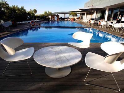 Moderner Außenbereich mit Pool, weißen Sesseln und einem runden Marmortisch auf Holzterrasse