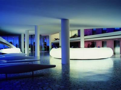 Moderner Hotelpool mit blauem und weißem Licht, umgeben von Säulen und einer offenen Architektur.