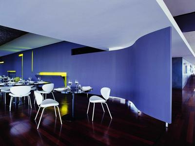 Moderner Innenraum mit lila Wand, weißen Stühlen und dunklem Holzboden in einem offenen Essbereich.