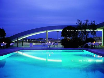 Beleuchteter Hotelpool bei Nacht mit modernem Dach und Sitzgelegenheiten.