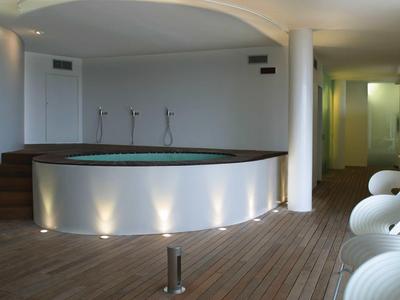 Moderner Wellnessbereich mit rundem Whirlpool, Holzboden und weißen Sitzgelegenheiten.