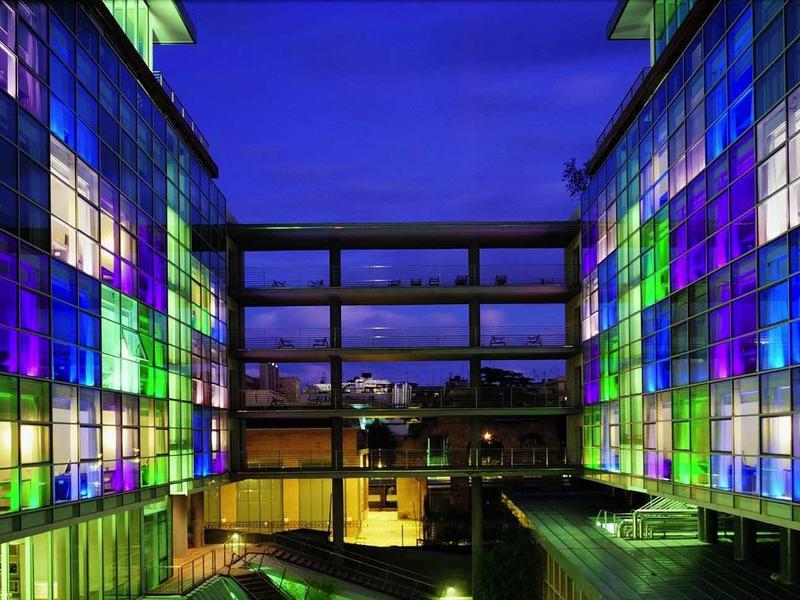 Moderne Gebäude mit bunten Glasfassaden in Blau, Grün und Violett bei Nacht.