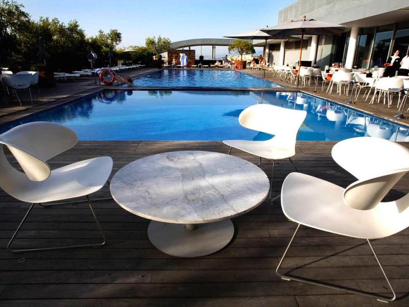 Moderner Außenbereich mit rundem Pool, weißen Stühlen und Tisch auf Holzterrasse bei Sonnenschein.