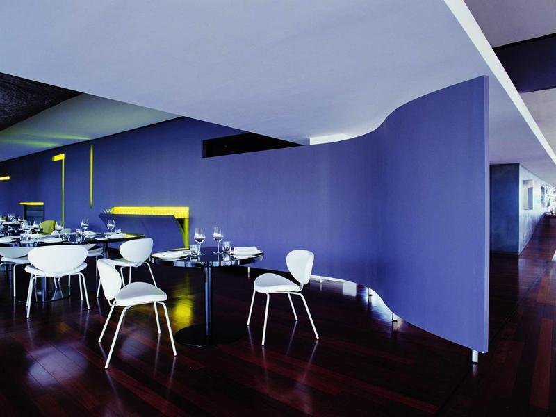 Moderner Innenraum mit lila Wand, weißen Stühlen und dunklem Holzboden in einem offenen Essbereich.