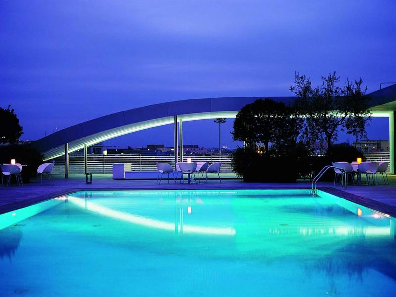 Beleuchteter Pool bei Dämmerung mit weißem Bogen und dunklem Himmel im Hintergrund.