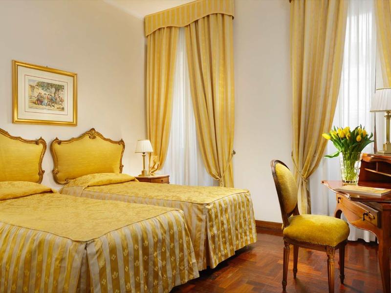 Elegancki pokój hotelowy z dwoma łóżkami pojedynczymi, złotą pościelą i klasycznym wystrojem.