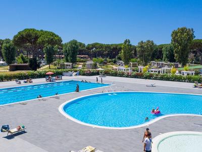 Groot buitenzwembad met helder water, ligstoelen en omliggend groen.