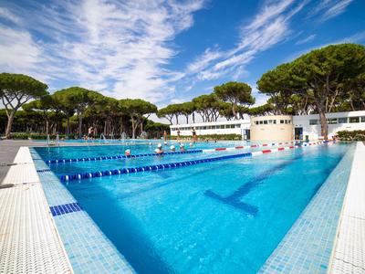 Piscine extérieure avec eau bleue claire, entourée d'arbres et d'un bâtiment en arrière-plan.