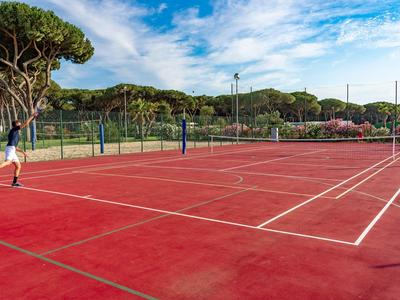 Terrain de tennis rouge en plein air avec des joueurs et des arbres en arrière-plan par temps ensoleillé