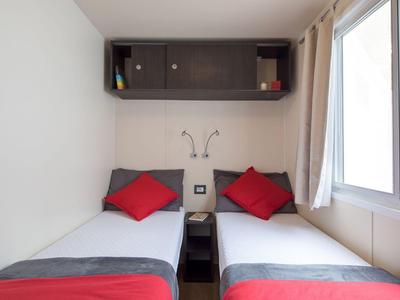 Kleine hotelkamer met twee eenpersoonsbedden, rode kussens en grijze beddengoed naast een raam.